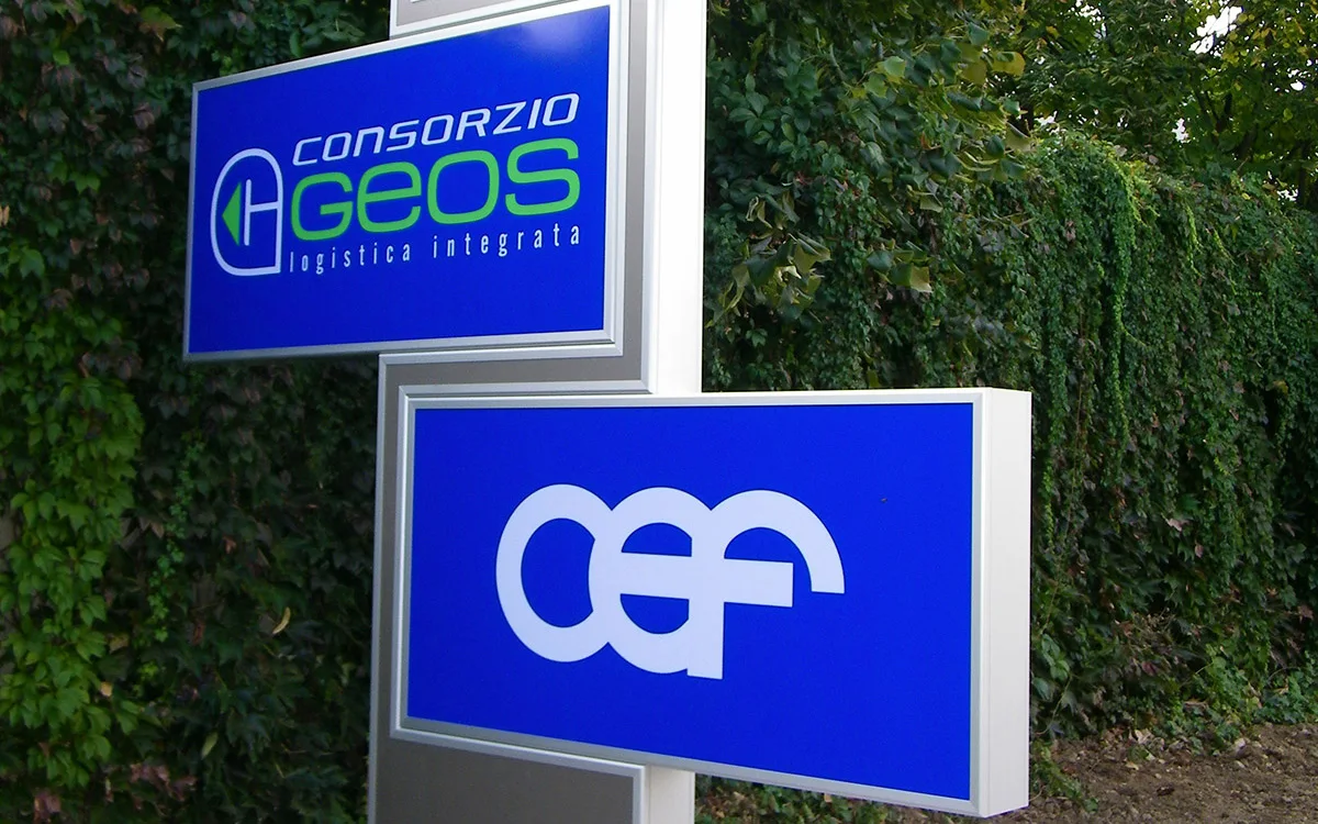 Insegne luminose a totem con logo aziendale su pannello retroilluminato per segnaletica esterna.
