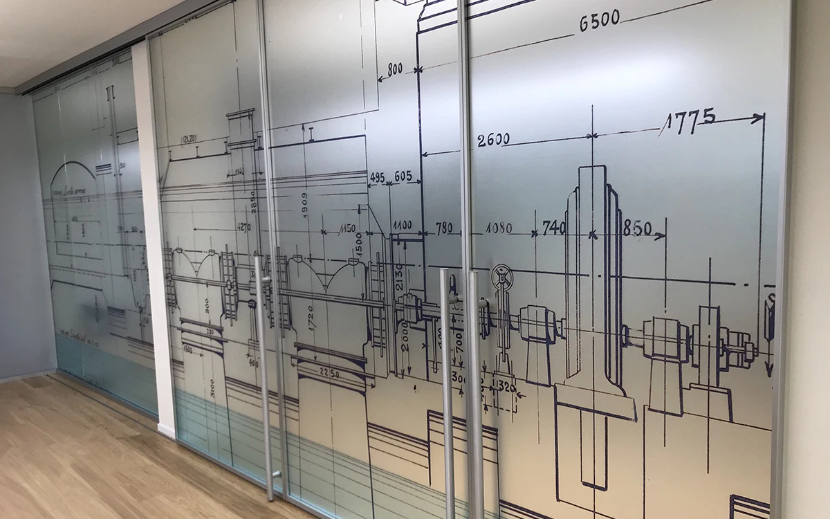 Pellicola decorativa su vetrata divisoria per ufficio con stampa disegno tecnico industriale.
