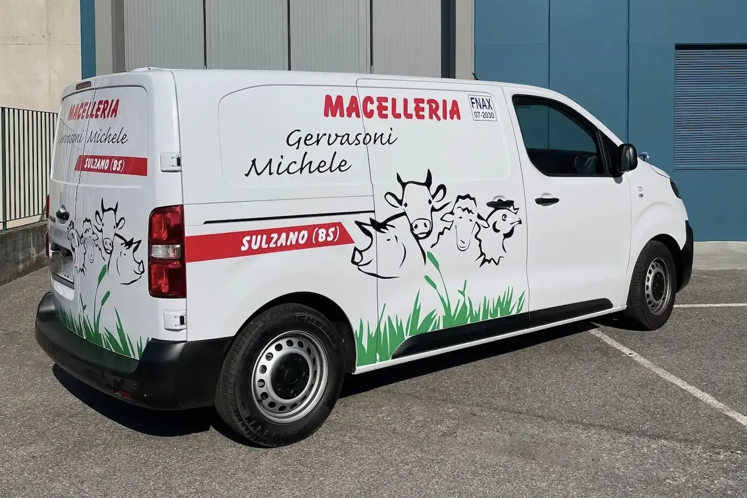 Furgone aziendale bianco con grafica laterale raffigurante illustrazioni di animali da fattoria e il nome della Macelleria Gervasoni Michele di Sulzano, in provincia di Brescia.