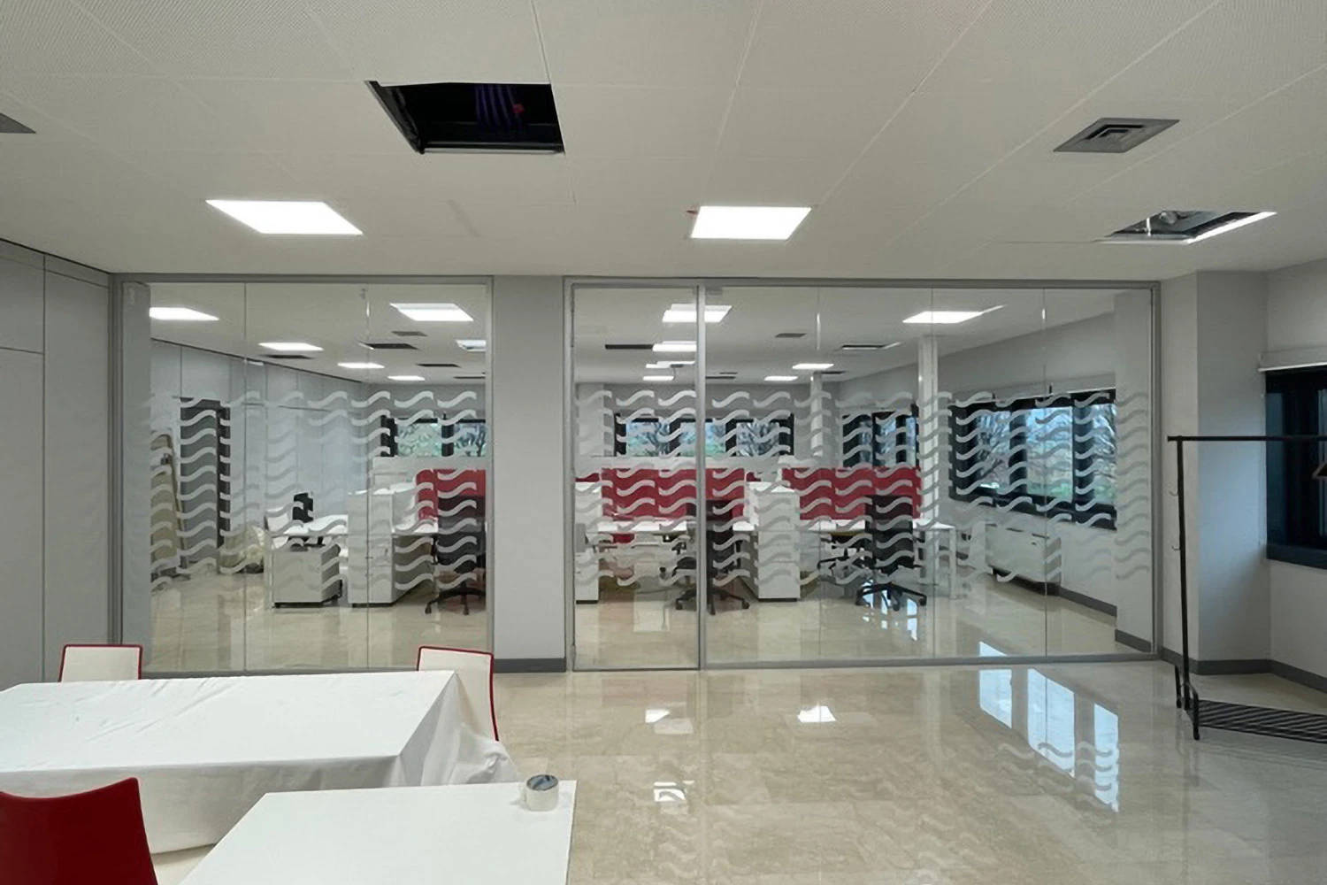 Sala riunioni moderna con pareti divisorie in vetro decorate con pellicola a motivo ondulato bianco e nero, sedie rosse, pavimento in marmo chiaro e illuminazione a pannelli a soffitto.