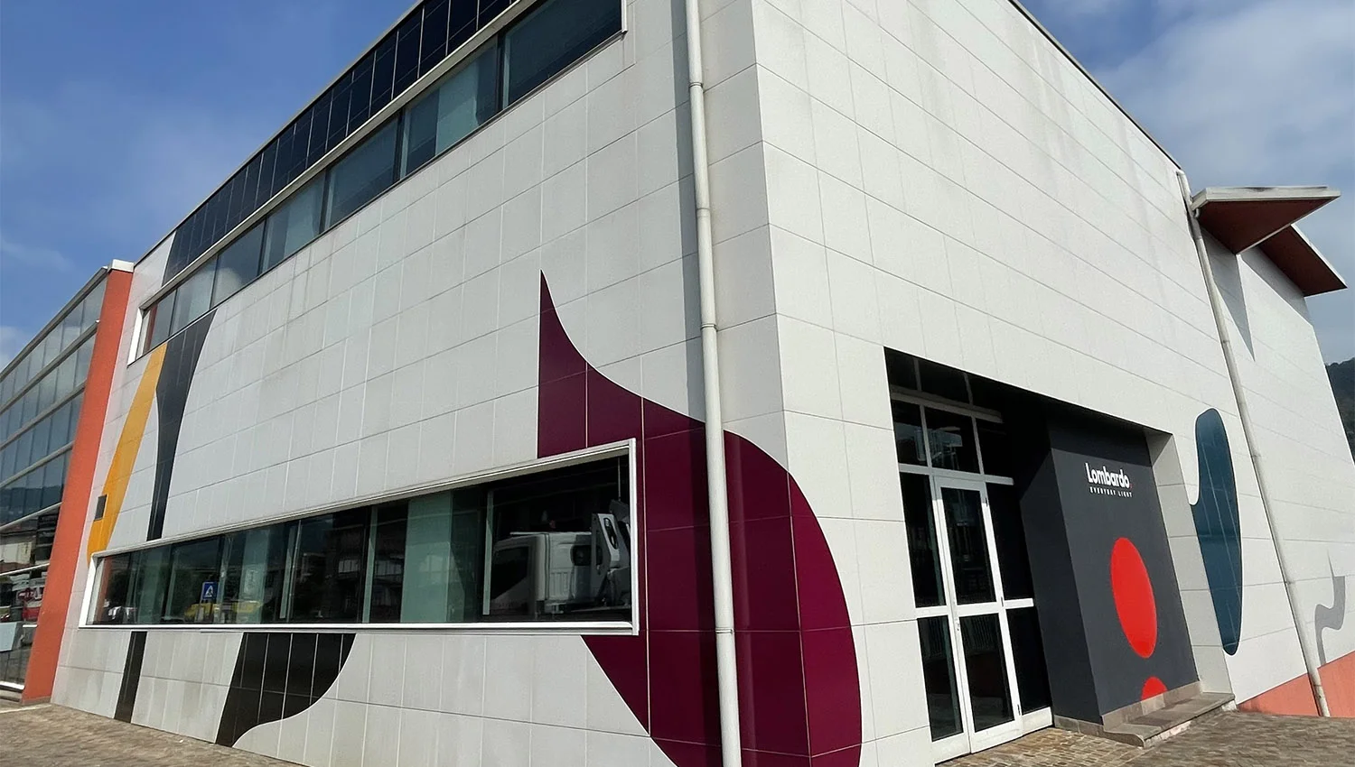 Decorazione esterna su facciata di edificio commerciale con grafiche geometriche adesive in bordeaux, arancione e rosso.